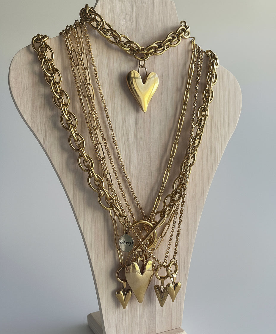 Gold chain necklaces with heart pendants on a wooden mannequin.